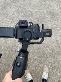 A compact DJI RS3 Mini gimbal stabilizer held by a videographer capturing smooth motion shots outdoors.