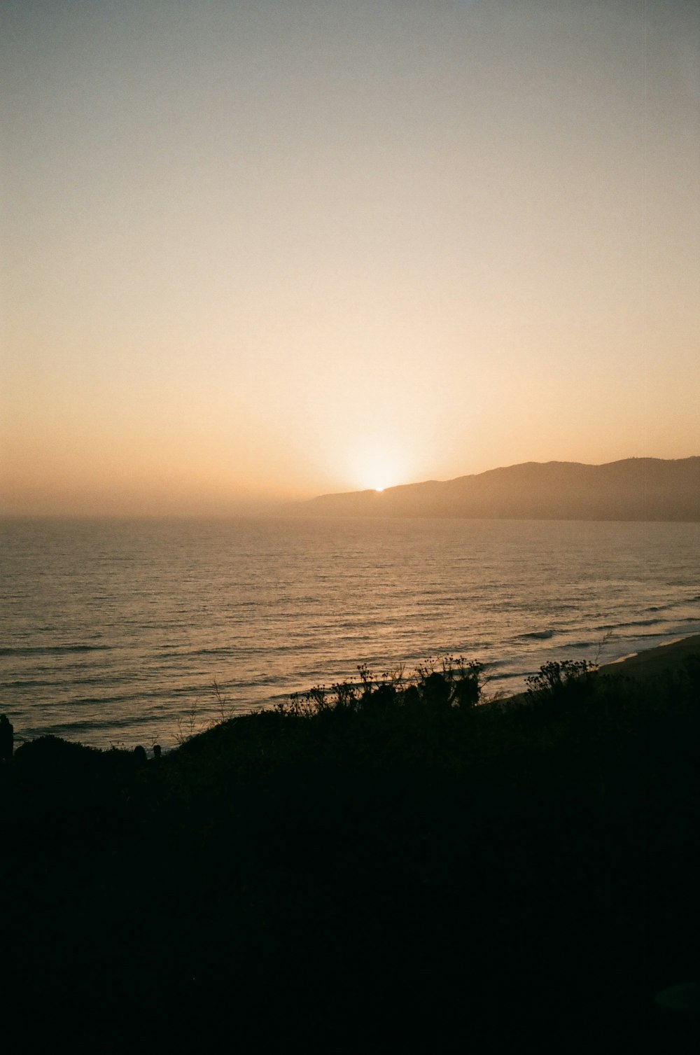 a body of water with a hill and a sunset in the background