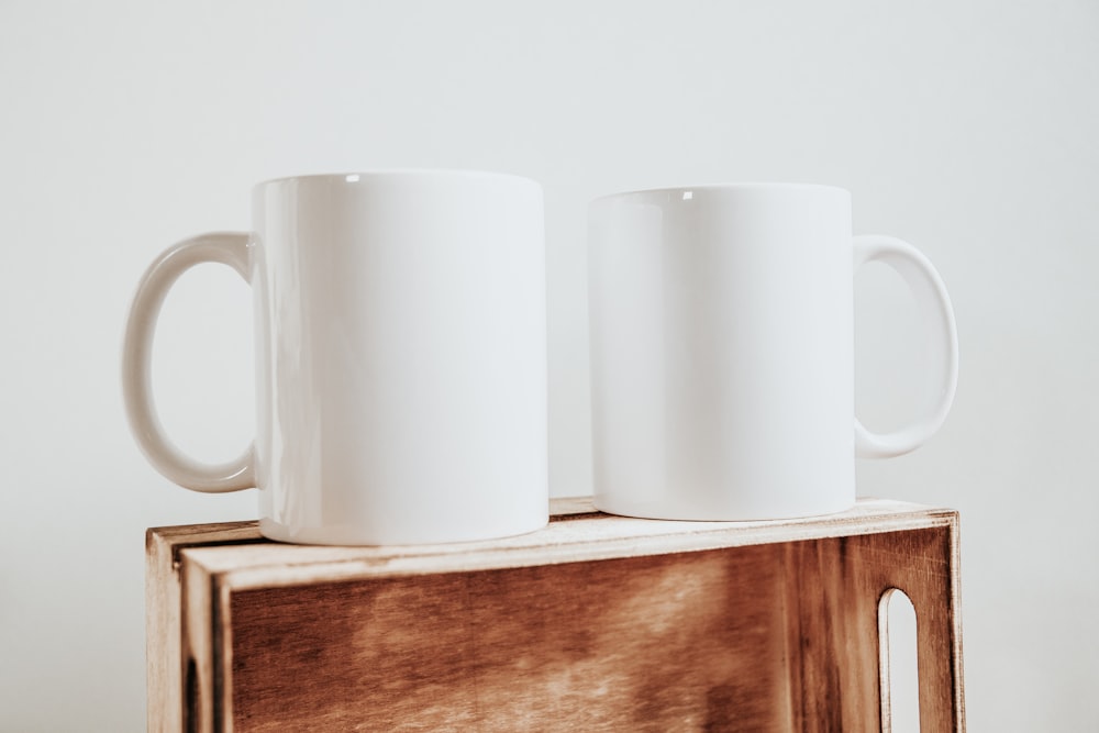 two white mugs on a wooden shelf