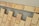 A pattern of rectangular beige bricks arranged on a layer of small gray gravel, interspersed with larger gaps. The surface appears to be under construction or preparation for a walkway or patio. The top edge features a lighter, lined surface, possibly for transitioning.