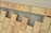 A pattern of rectangular beige bricks arranged on a layer of small gray gravel, interspersed with larger gaps. The surface appears to be under construction or preparation for a walkway or patio. The top edge features a lighter, lined surface, possibly for transitioning.