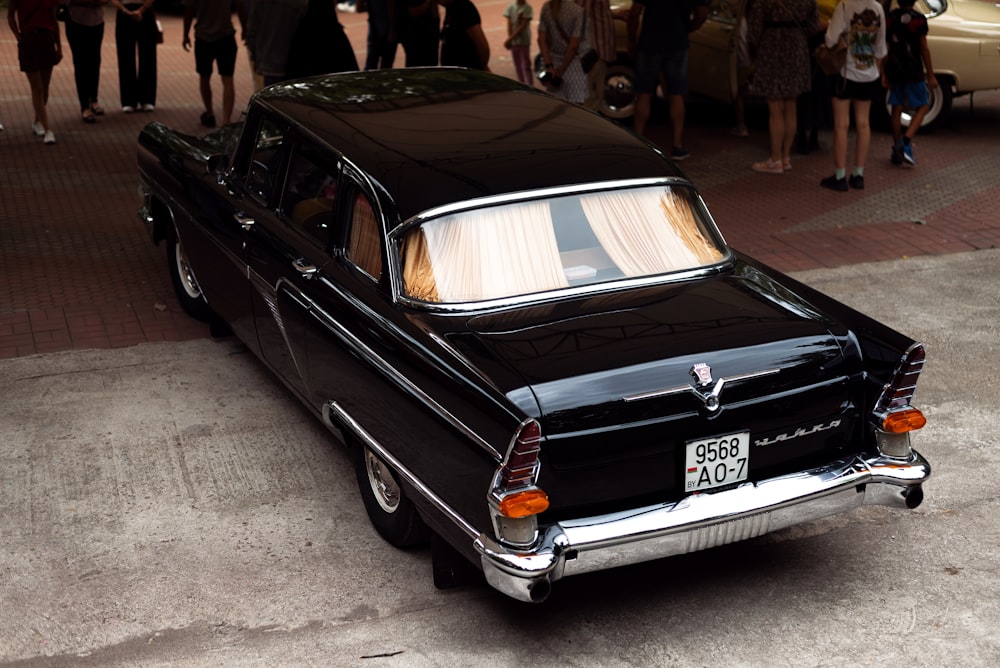 a black car parked on a brick road with people walking around