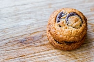 Two chocolate chip cookies stacked on a wooden surface, showcasing a golden-brown texture with visible chunks of chocolate.