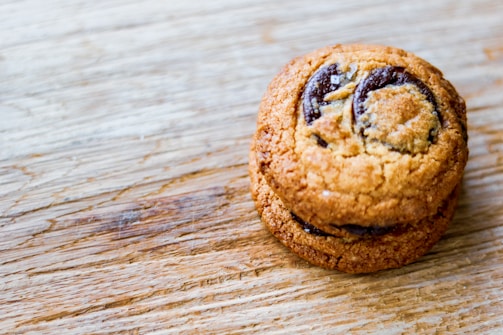 A close-up of golden-brown chocolate chip cookies stacked on a rustic wooden table.