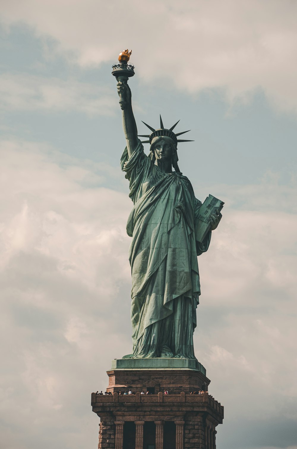 eine Statue einer Person, die eine Fackel mit der Freiheitsstatue im Hintergrund hält