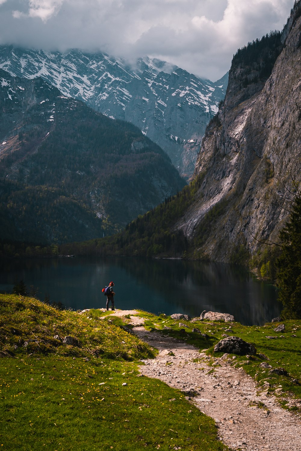 a person standing on a trail by a lake with mountains in the background
