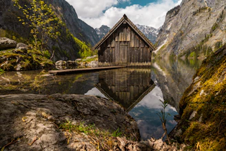 Rustic cabin with a stone chimney beside a tranquil lake reflecting the sunset.