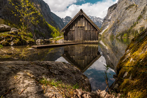Rustic cabin with a stone chimney beside a tranquil lake reflecting the sunset.