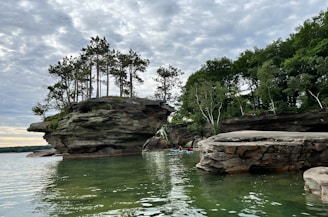 A couple launching their kayak from a rocky lakeshore surrounded by pine trees during sunrise