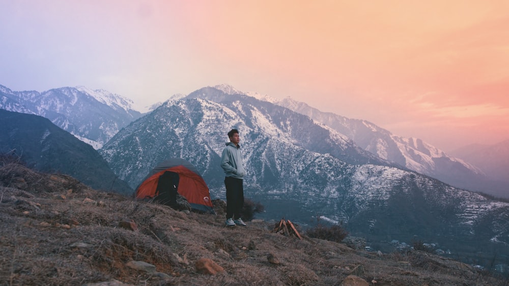 a man standing next to a tent on a mountain