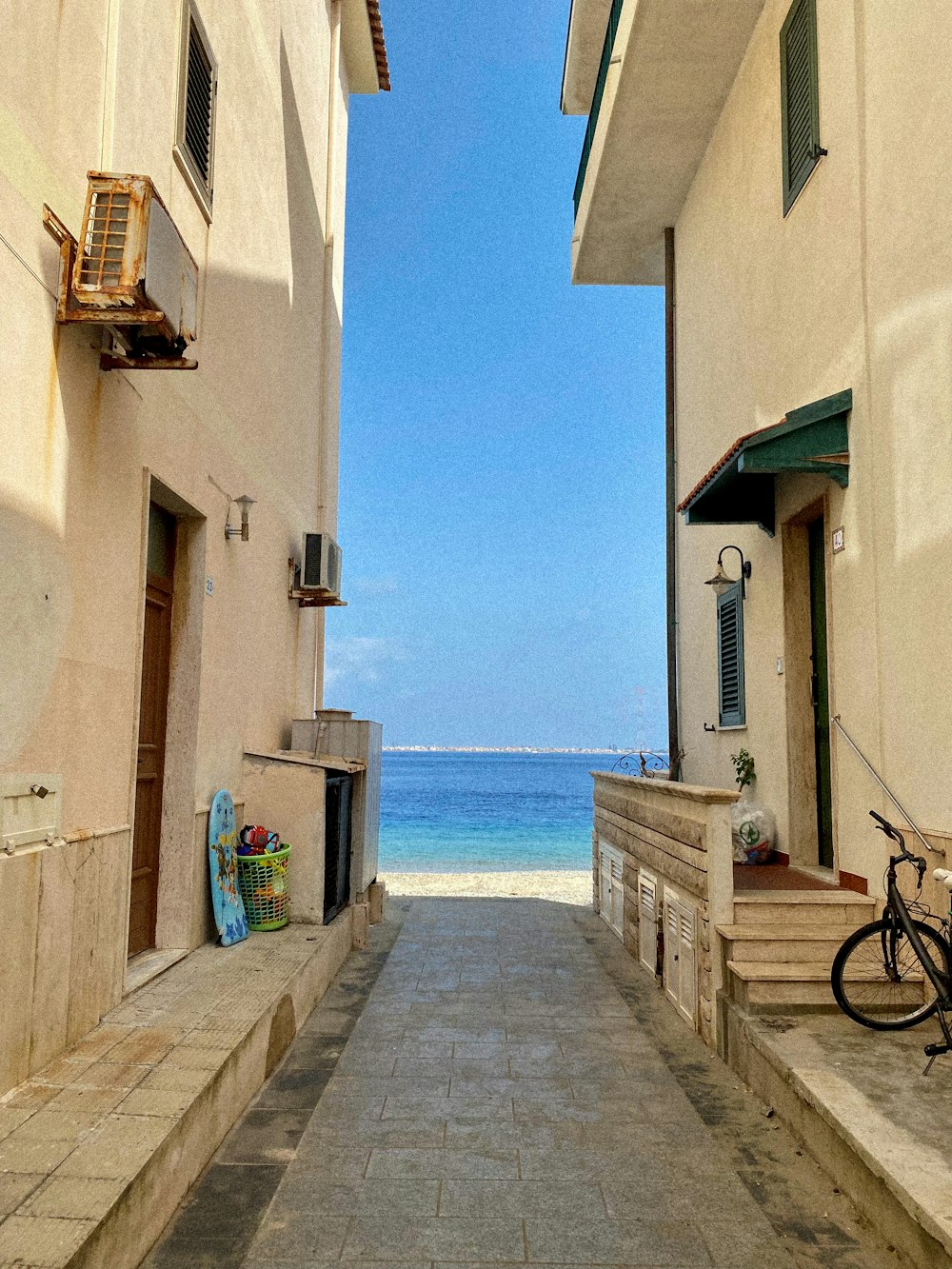 a path between buildings with a body of water in the background