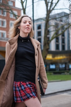 A stylish woman in a soft beige trench coat walking confidently down a city street, with a blurred urban background highlighting her chic outfit.