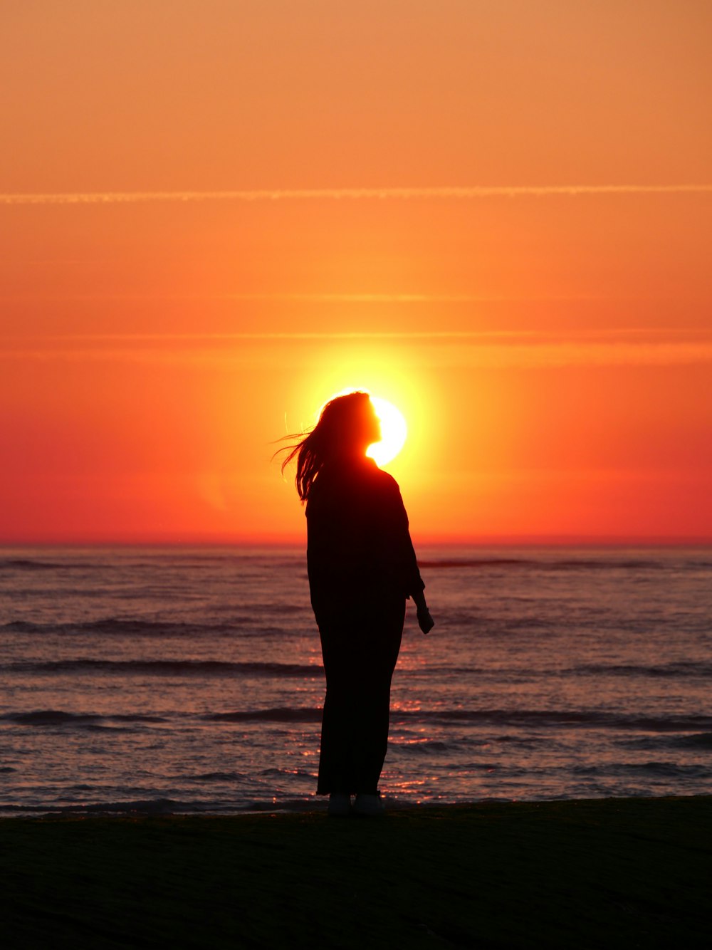 a man standing on a beach with the sun setting behind his