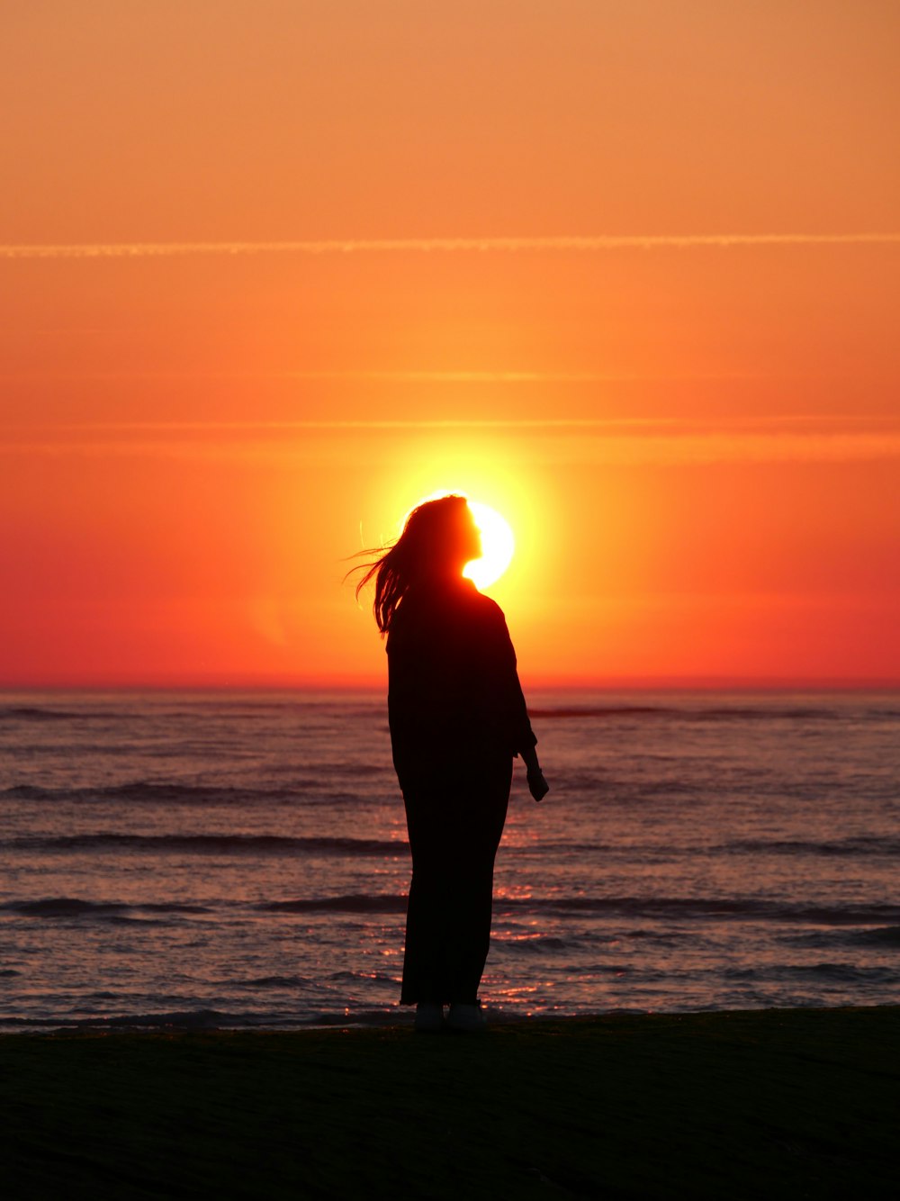 Un uomo in piedi su una spiaggia con il sole che tramonta dietro di lui