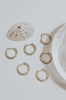 Minimalist gold stud earrings arranged artfully on a smooth ivory surface with soft shadows.