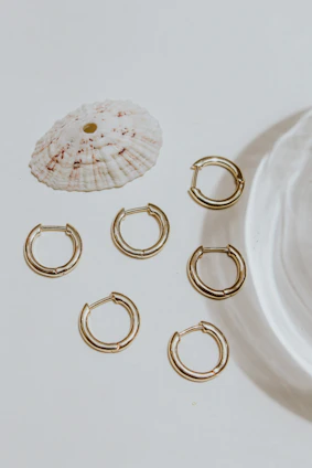 Delicate gold and nude tone earrings arranged artistically on a light textured surface.