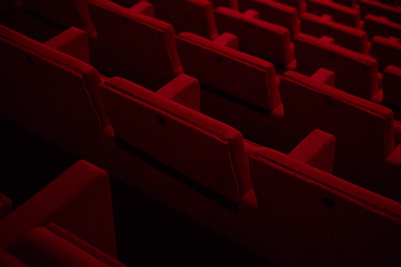 Rows of red cushioned theater seats arranged in a pattern. The lighting is dim, suggesting a cinema or auditorium setting.