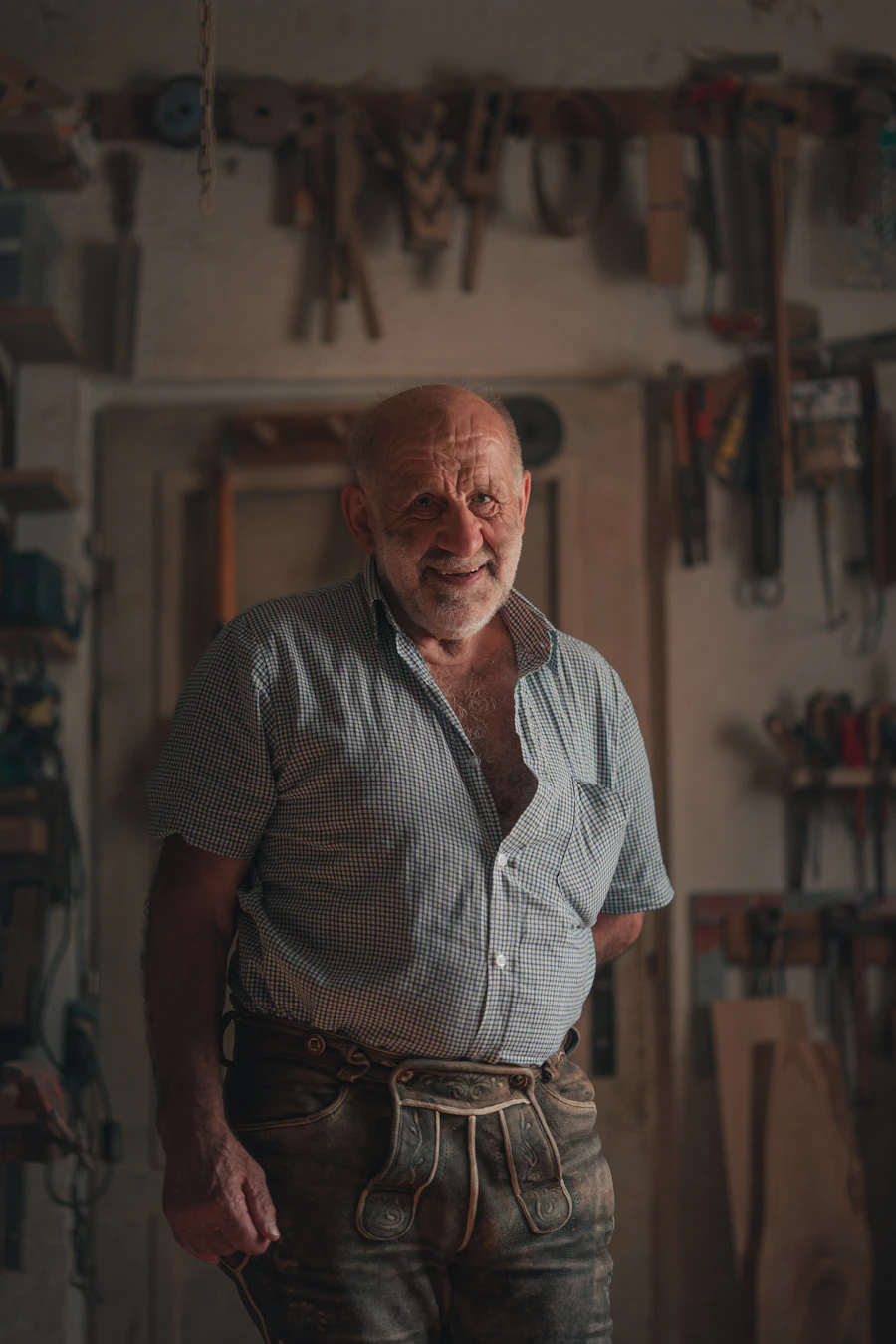 An older man standing in a workshop in front of a wall of tools