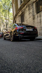 A sleek black luxury car parked with a sharply dressed professional driver standing confidently beside it.