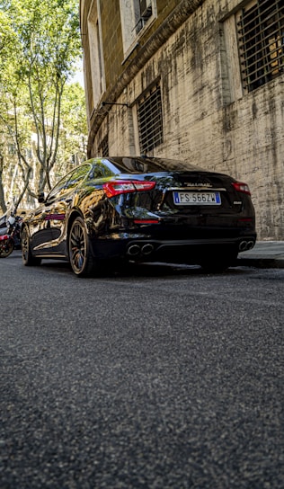 A sleek black luxury car with a professional driver standing beside it in an urban Jakarta setting.