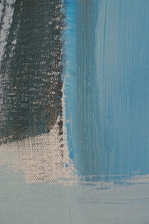 A close-up view of an abstract painting featuring textured brushstrokes. The canvas is dominated by shades of blue and dark gray, with visible strokes and layers overlapping each other. The texture of the canvas adds depth, and there is a rough transition between colors.