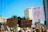 A group of people participates in a protest, holding signs advocating for reproductive rights and healthcare. The background features tall buildings and clear blue skies. Numerous signs have written messages such as 'Reproductive Rights are Human Rights,' 'Abortion = Healthcare,' and 'My Pussy My Choice.'