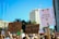 A group of people participates in a protest, holding signs advocating for reproductive rights and healthcare. The background features tall buildings and clear blue skies. Numerous signs have written messages such as 'Reproductive Rights are Human Rights,' 'Abortion = Healthcare,' and 'My Pussy My Choice.'