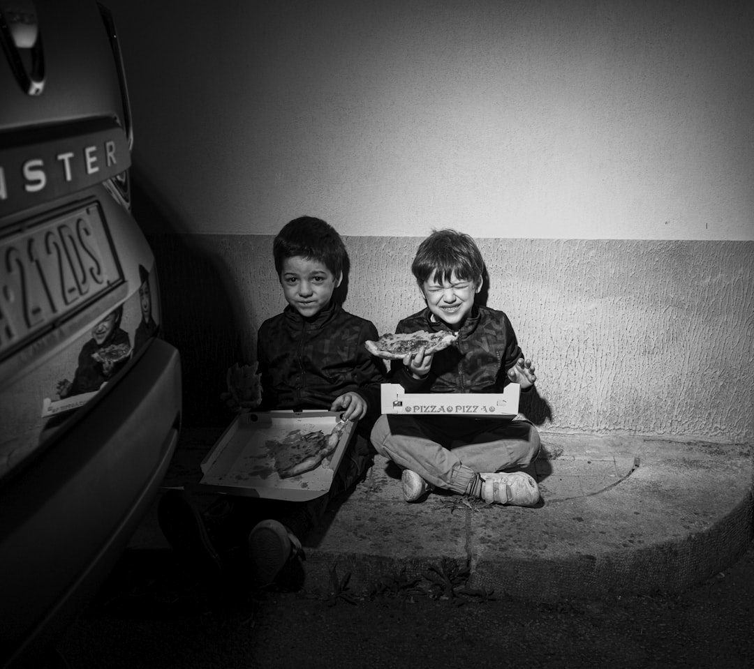 two children sitting on steps, A couple of children eating pizza sitting on a sidewalk in Italy.