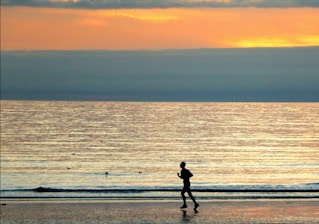 A warm sunset scene with a man in his 40s jogging along a peaceful beach path, radiating energy and motivation.