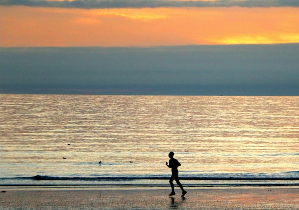 A sunrise jog along a quiet beach with palm trees silhouetted against the orange sky.
