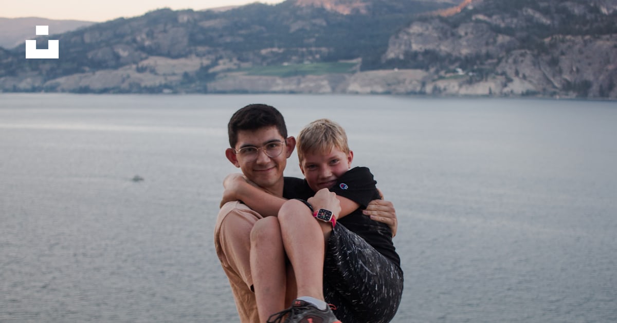 A man holding a baby on a rock by a body of water photo – Free Portrait ...