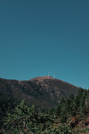 Wind turbines spinning smoothly on a green hillside with a bright blue sky