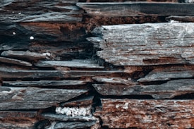 A close-up view of stacked, weathered stone slabs, showcasing a variety of rough and uneven textures. The stones are layered horizontally and display natural striations and color variations.