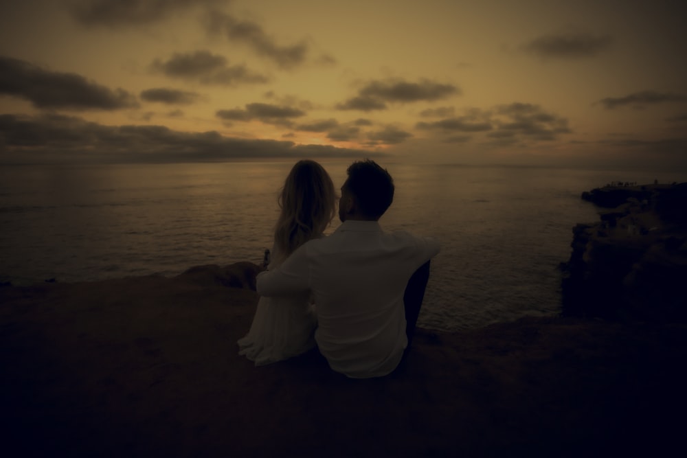 a man and woman sitting on a beach looking at the water