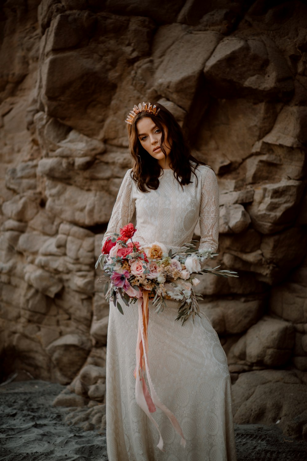 a woman in a white dress with a crown and flowers in front of a rock wall