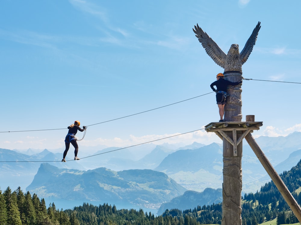 a couple of people climbing a wooden tower with a mountain in the background
