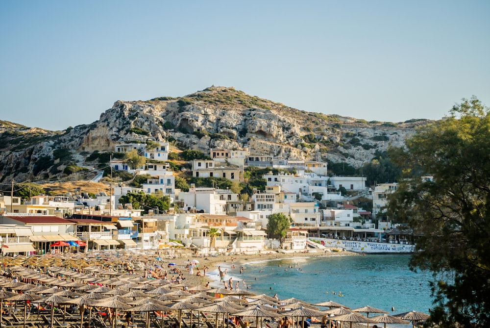 a beach with many people and umbrellas by a body of water