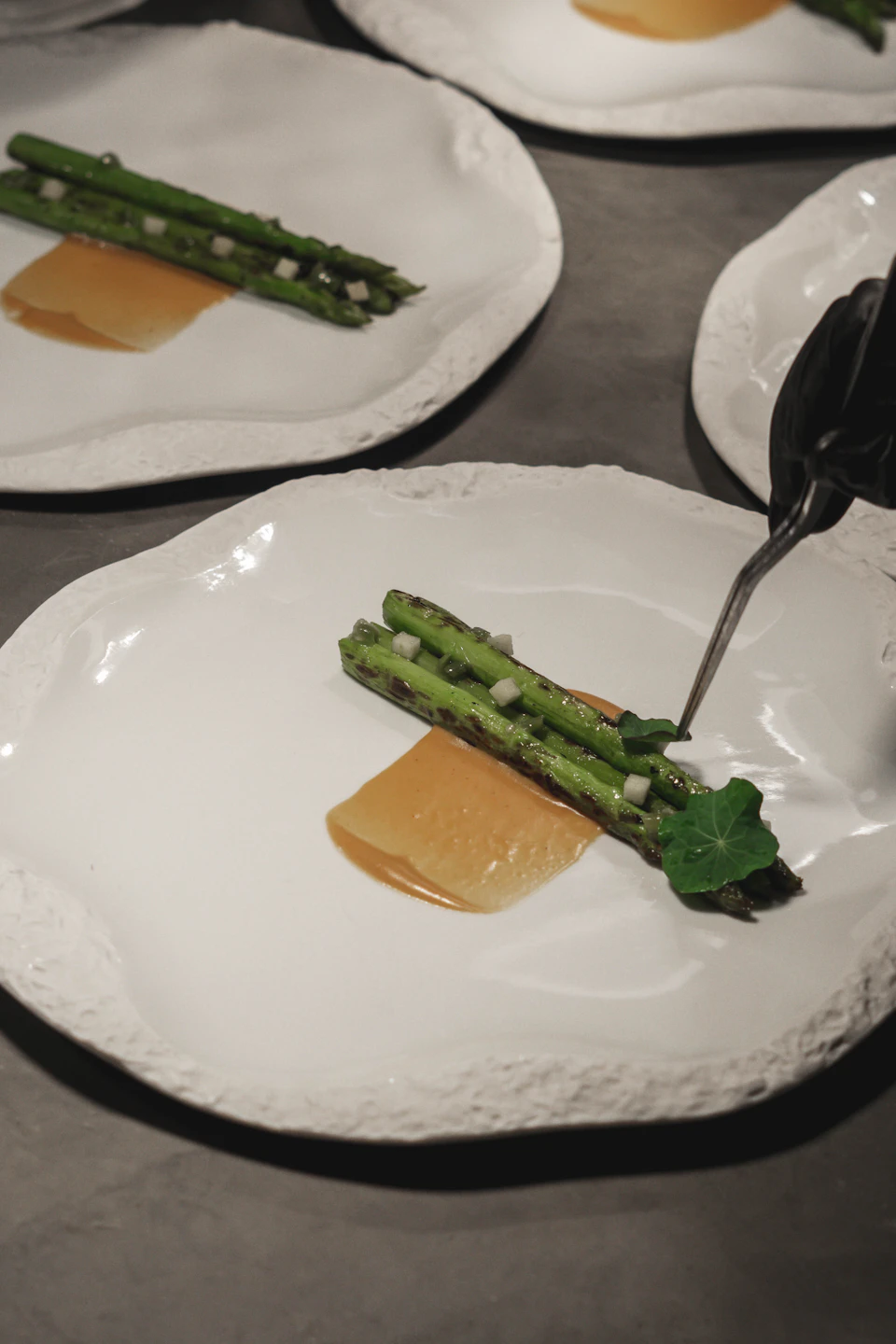 Green asparagus arranged on a plate with sauce and garnished parsley, on a gray countertop