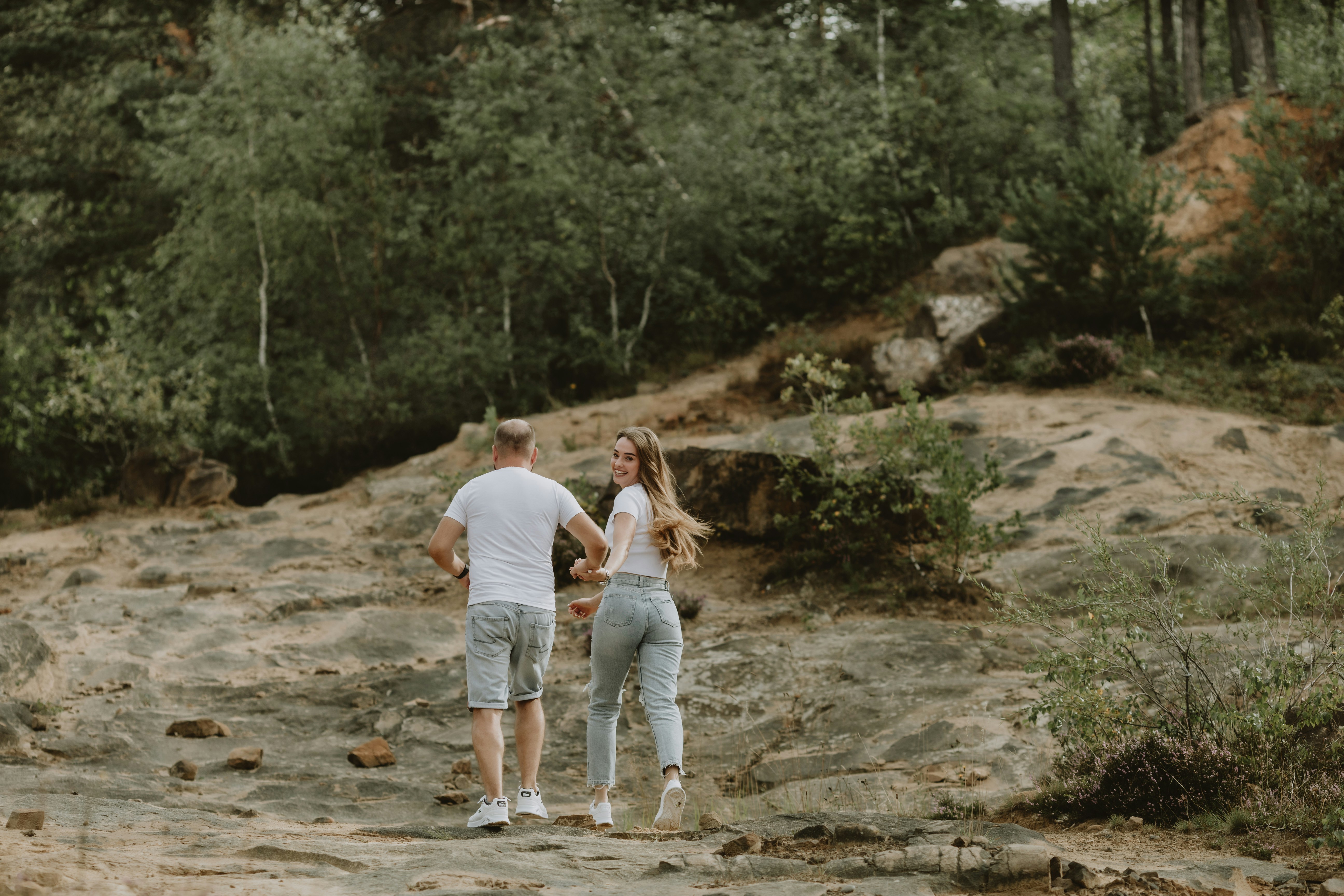 a man and woman walking on a dirt path in the woods