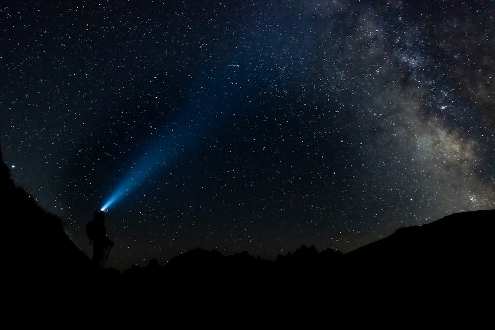 uma pessoa de pé em uma montanha com um céu estrelado acima