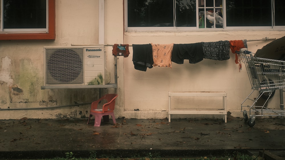 a red chair next to a white building with clothes outside