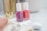 Two bottles of nail polish in pink and coral shades are placed on a light-colored surface. They are surrounded by soft-focus objects such as a gold cylindrical container and a folded pink towel, creating a cozy and elegant ambience.