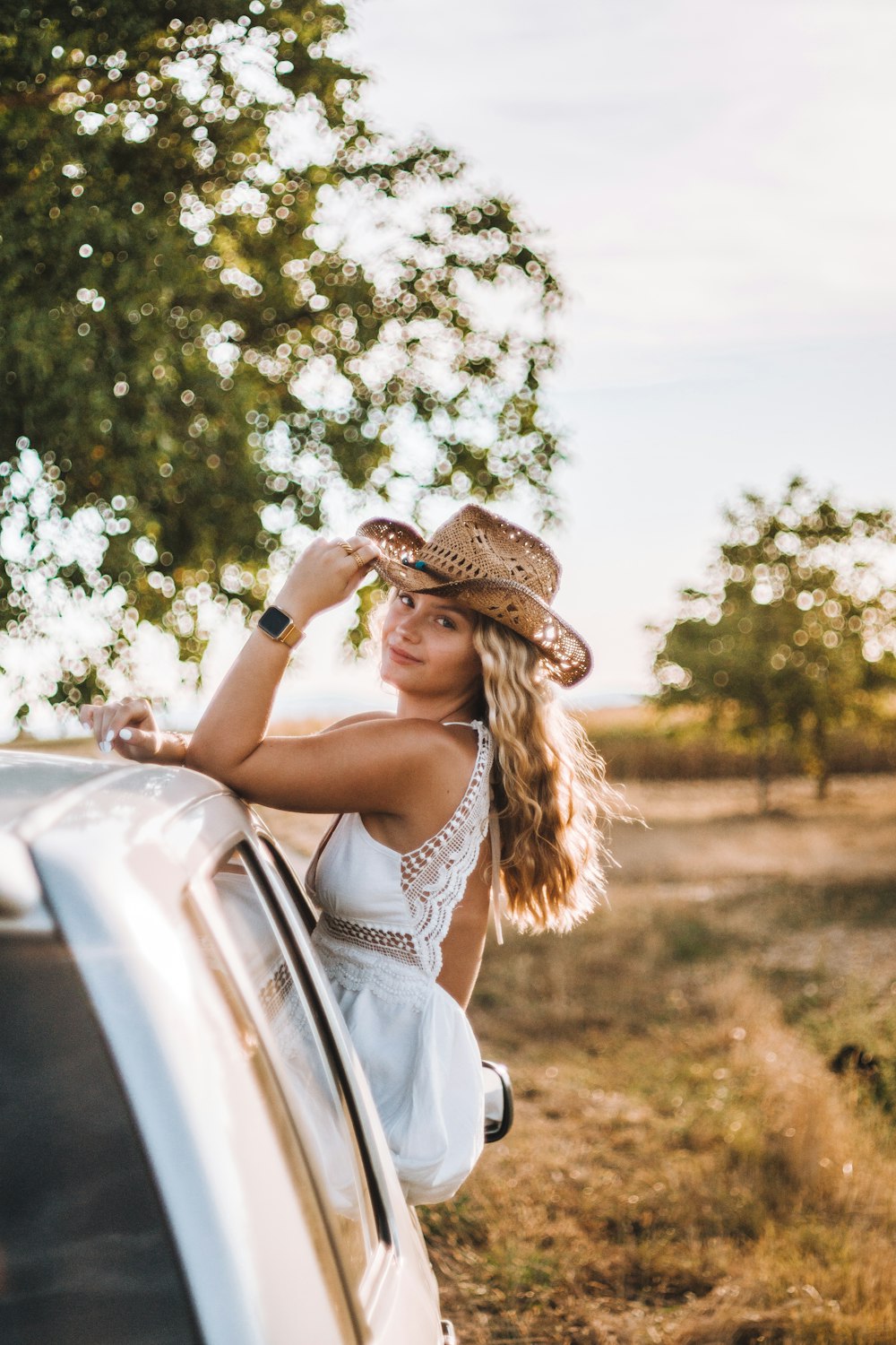 a woman in a hat leaning on a car