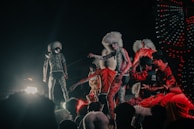 Performers dressed in tiger-like costumes with white furry headpieces engage in a vibrant street parade or performance, surrounded by a crowd. The scene is filled with colorful lights and dynamic movement.