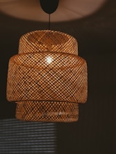 Woven rattan pendant lamp detail with warm lighting casting intricate shadows on surrounding surfaces.