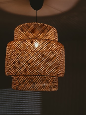 Woven rattan pendant lamp detail with warm lighting casting intricate shadows on surrounding surfaces.