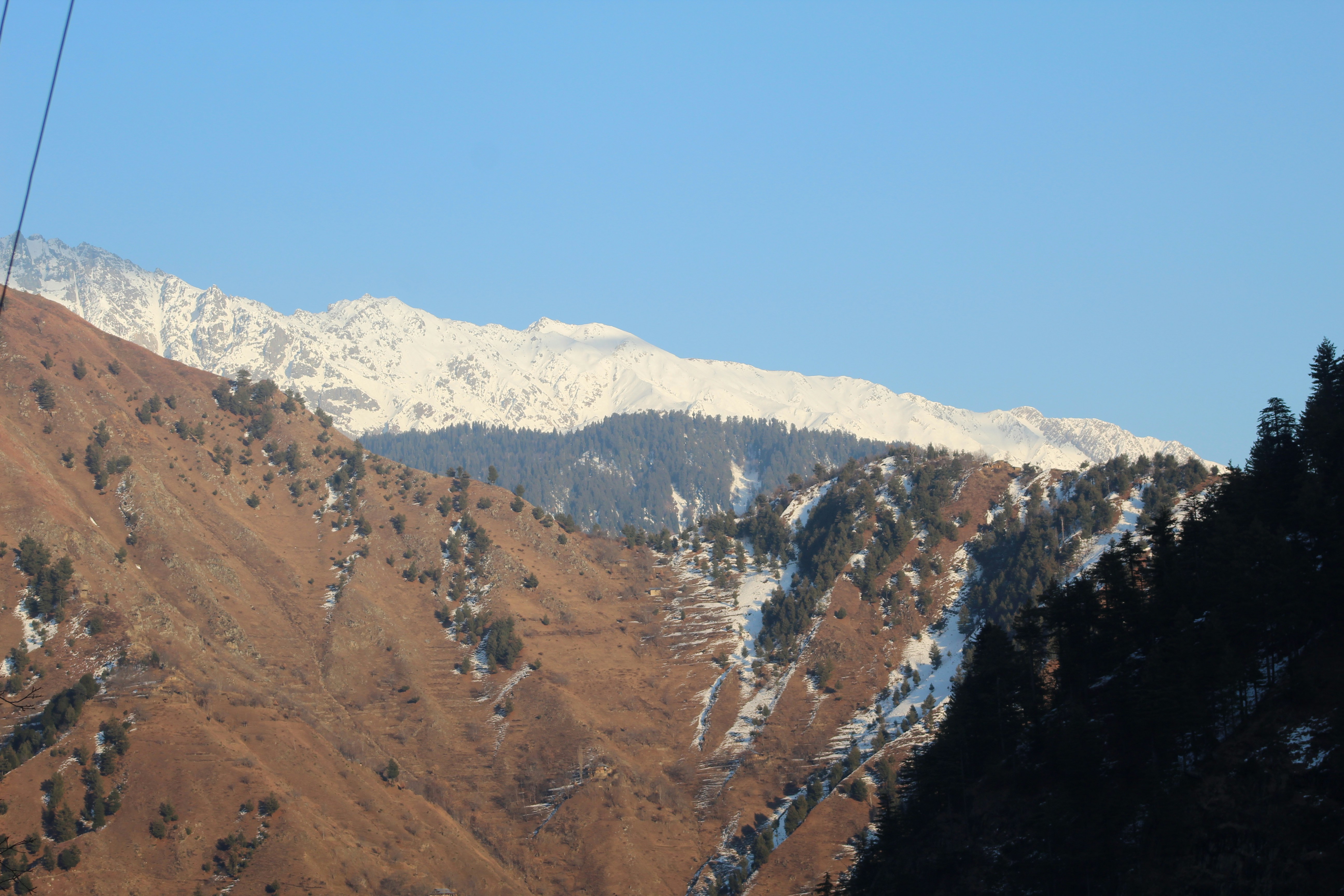 A wide shot of a snow-capped mountainous region in Kashmir with a small village nestled in the valley, symbolizing remote areas needing local representation.