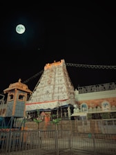 Front view of Sri Sorakayala Swamy Temple adorned with glowing lamps and maroon-gold decorations at dusk.