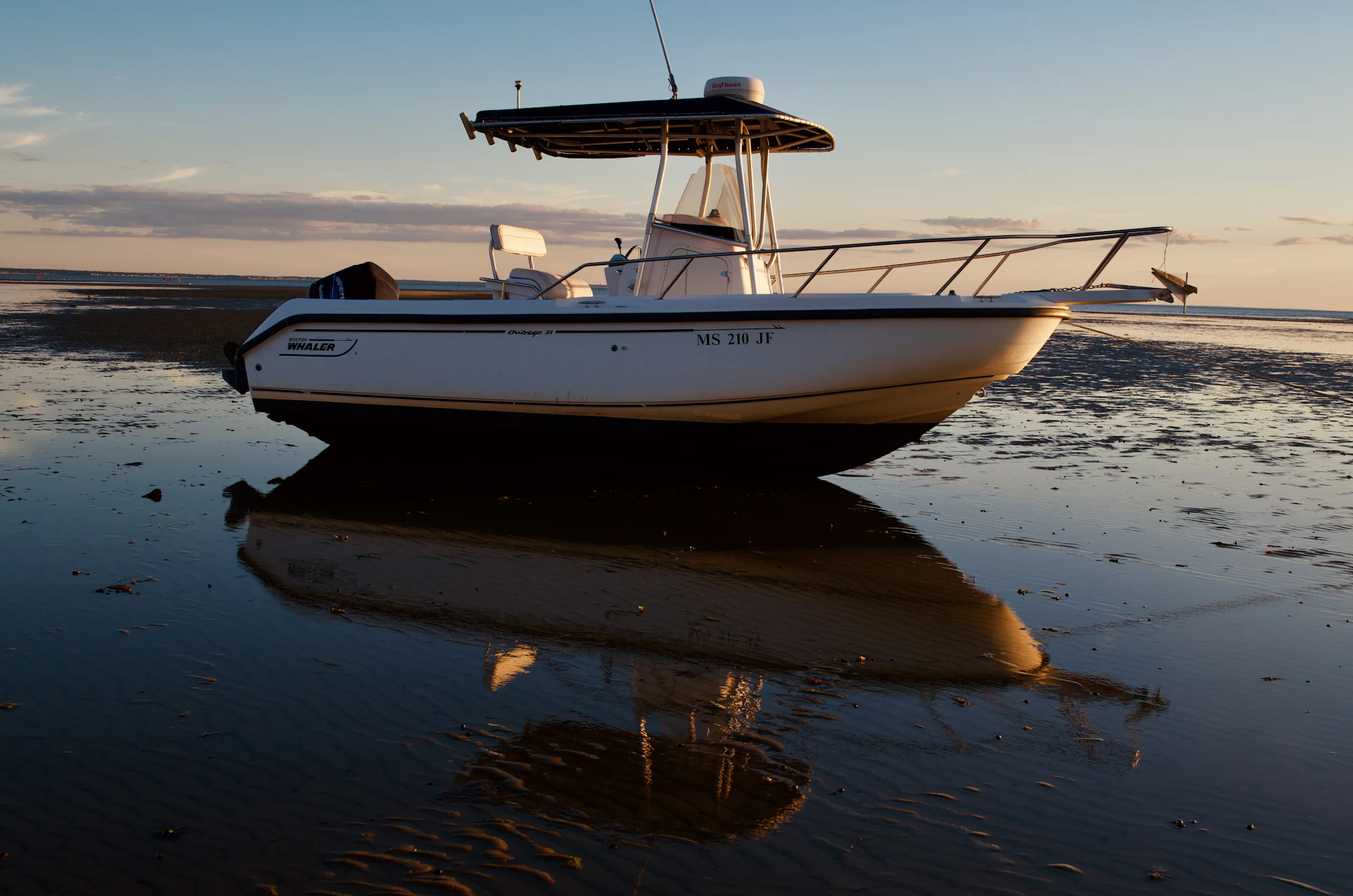A boat sitting on glassy water at sunset with its reflection below it