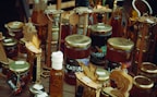 A variety of jars and bottles displaying honey, dried fruits, and other artisanal products. The jars are arranged on a wooden surface, with decorative wooden signs and labels highlighting the contents. The products appear to be homemade or locally sourced, giving an artisanal and rustic vibe.